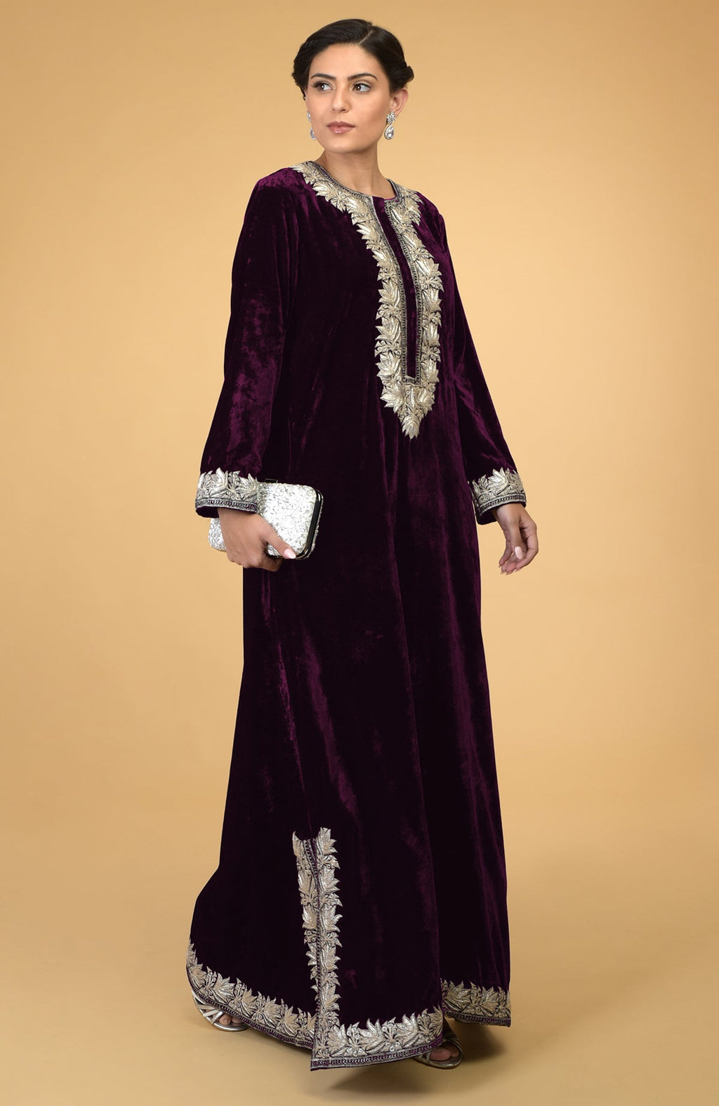 Plum velvet kaftan with silver Kashmir embroidery, held by a woman with a white clutch.