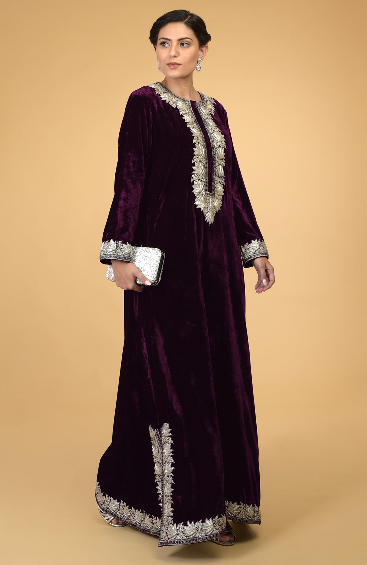 Plum velvet kaftan with silver Kashmir embroidery, held by a woman with a white clutch.