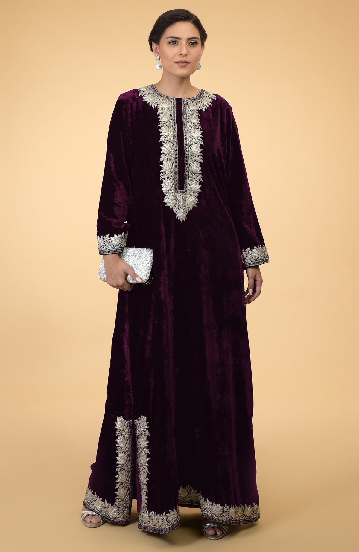 A woman models a plum velvet kaftan with silver Kashmir embroidery and a white clutch.