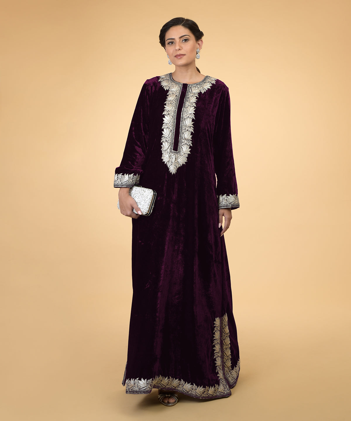 Plum velvet kaftan with silver Kashmir embroidery, held by a woman with a white clutch.