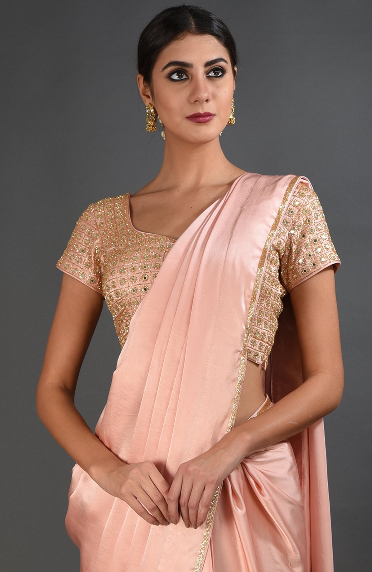 A woman models a pearl pink satin silk saree with mirror and zardozi embroidery.
