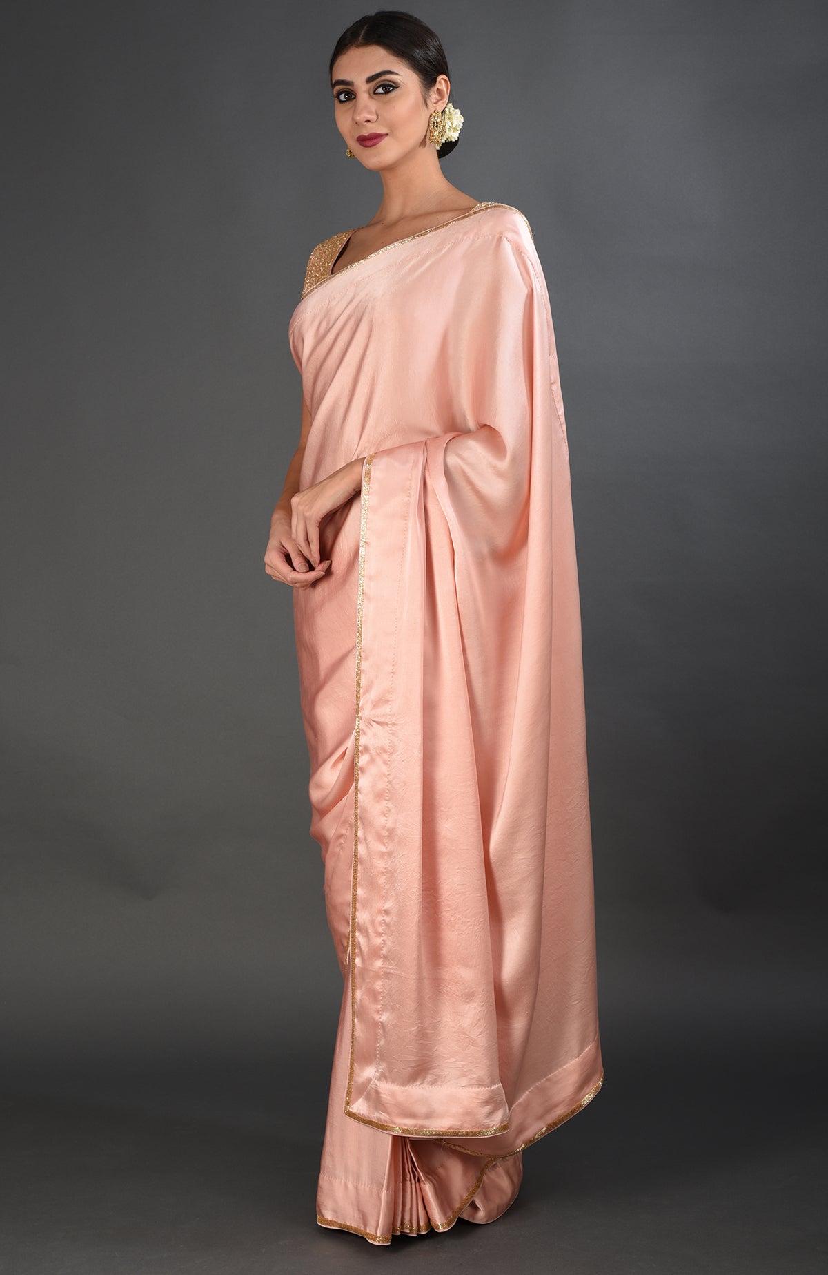 A woman models a pearl pink satin silk saree with gold borders and a matching blouse.