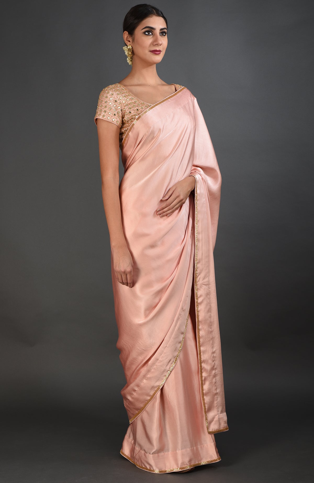 A woman models a pearl pink satin silk saree with mirror and zardozi embroidery.