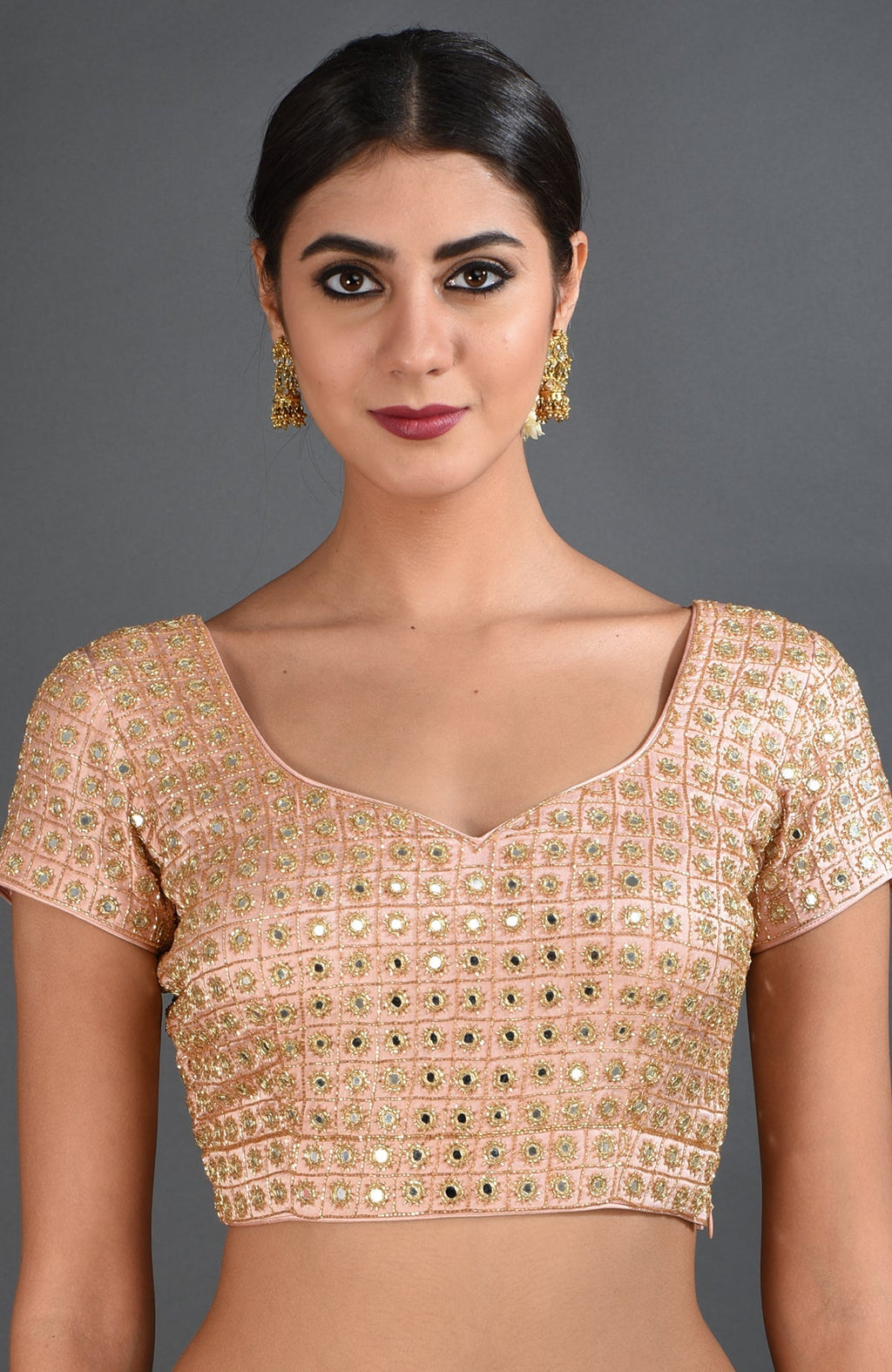 A woman models a pearl pink mirror work and zardozi hand embroidered blouse.