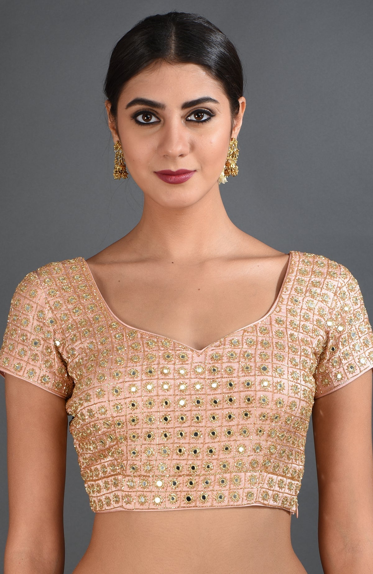 A woman models a pearl pink mirror work and zardozi hand embroidered blouse.