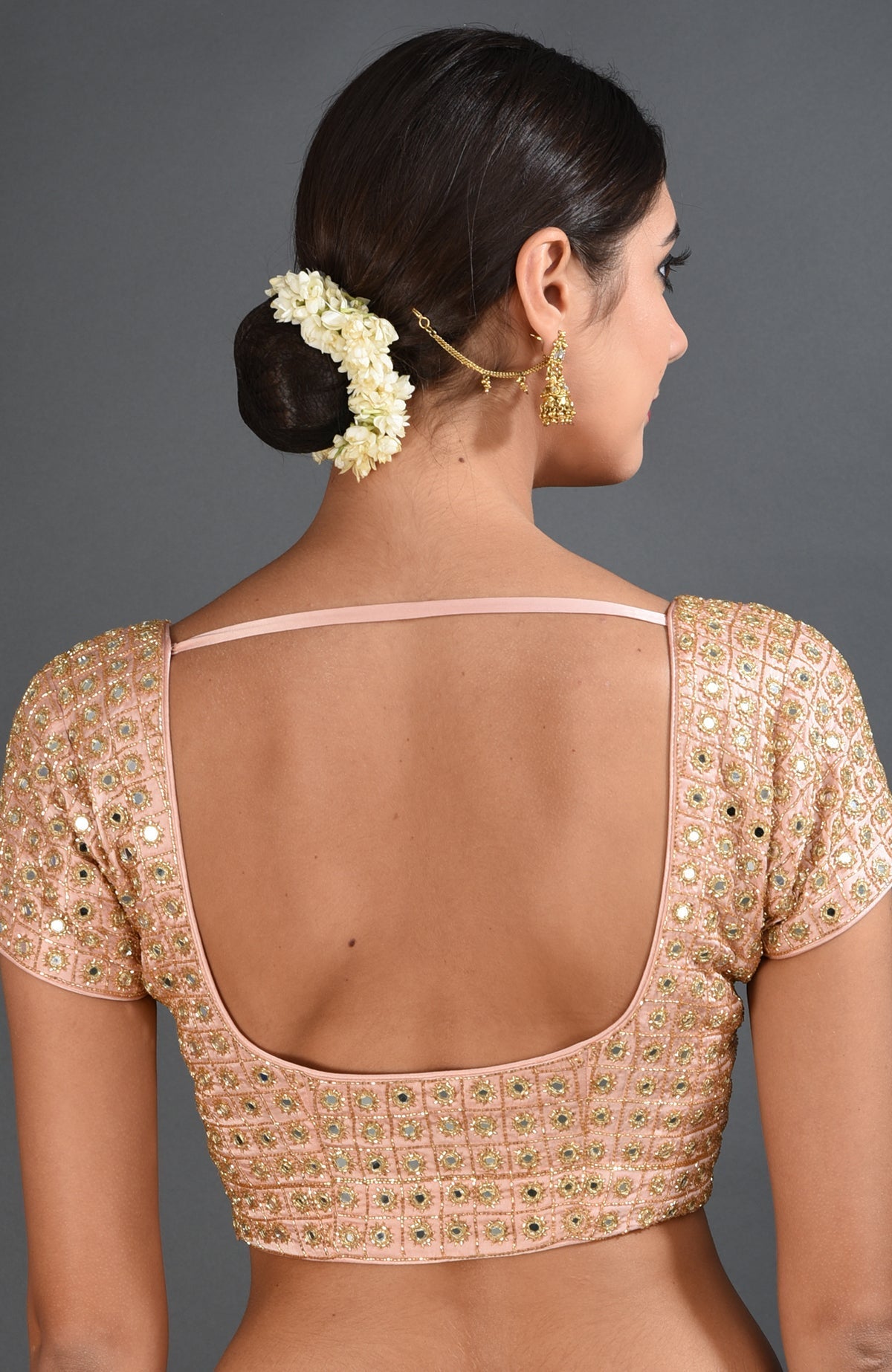 A woman from behind wearing a pearl pink mirror work and zardozi hand embroidered blouse.