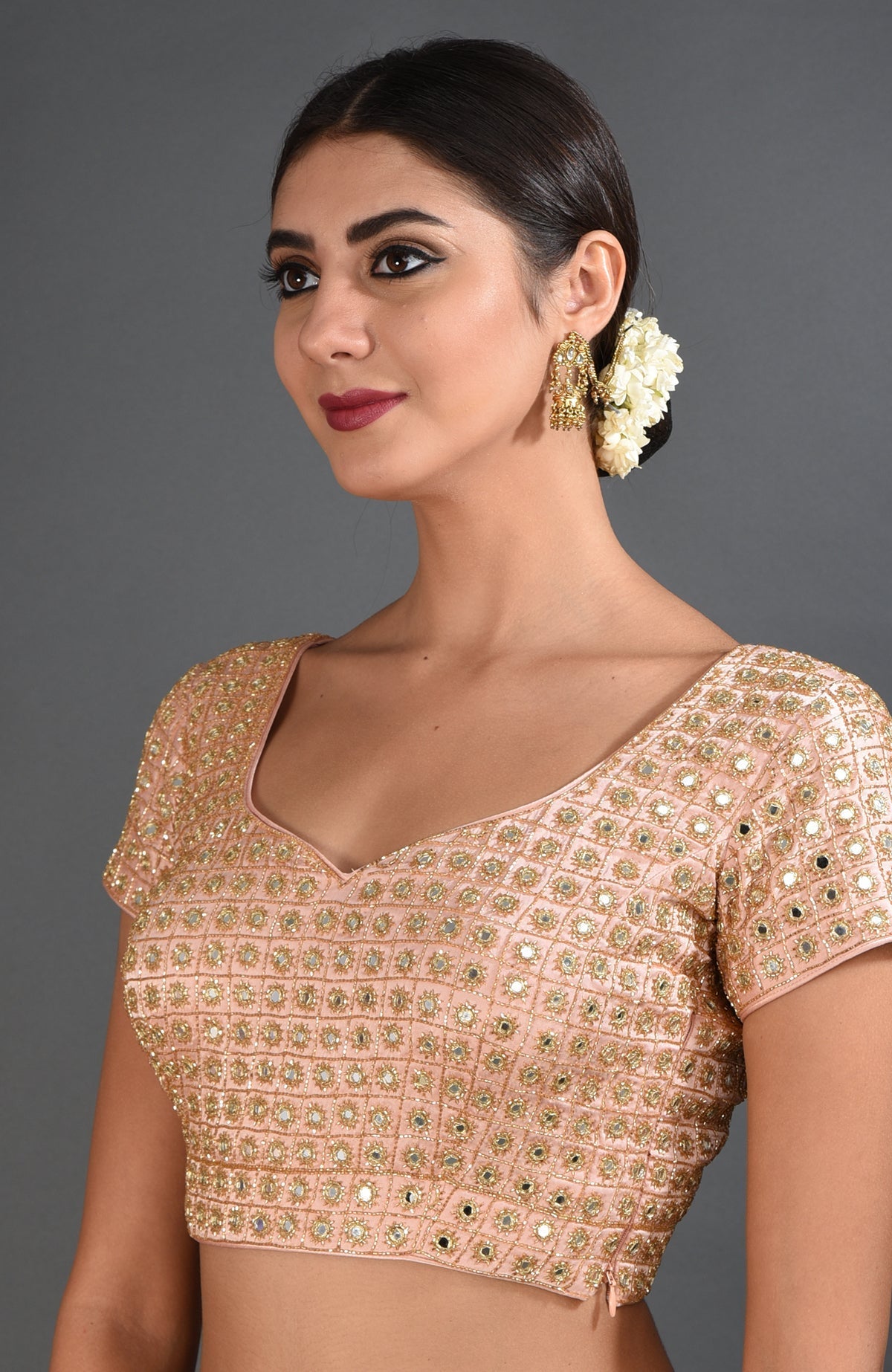 A woman models a pearl pink mirror work and zardozi hand embroidered blouse.