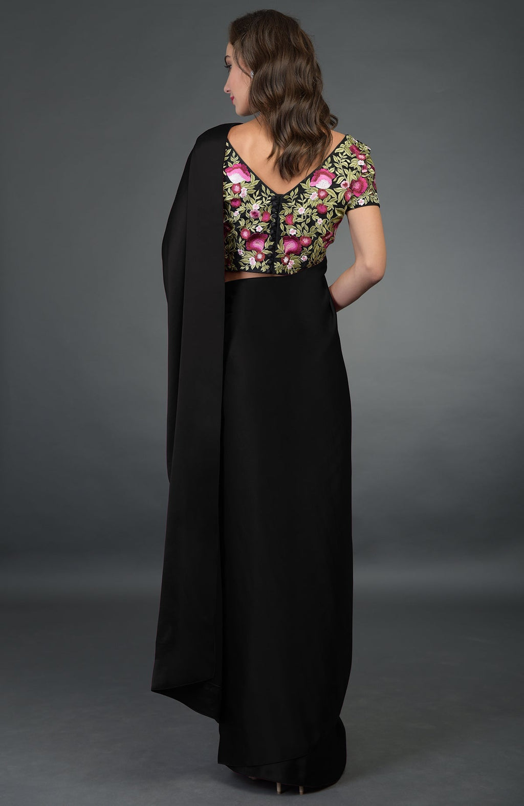 A woman models a black saree with a floral embroidered blouse from the back.