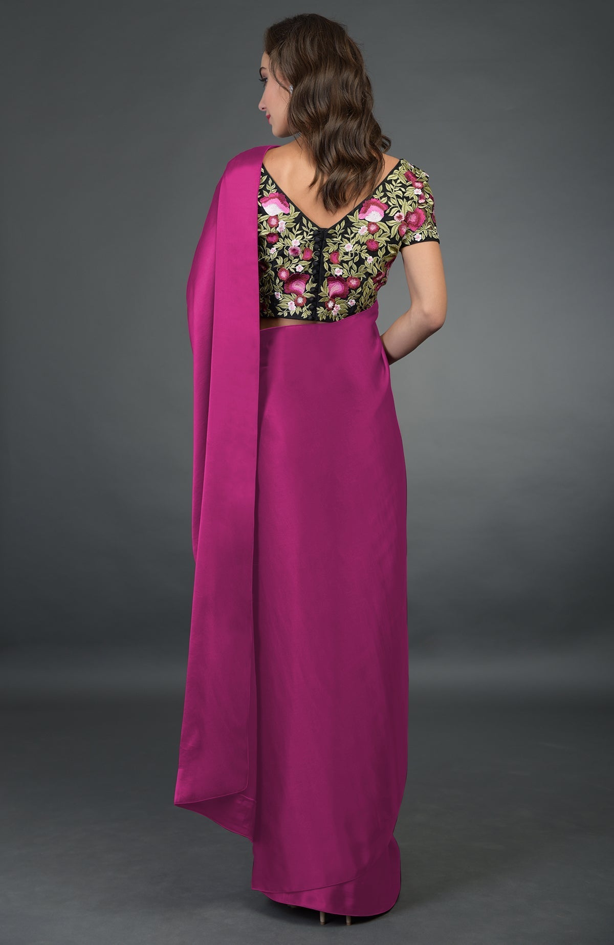 A woman models a raspberry saree with a black floral embroidered blouse from the back.