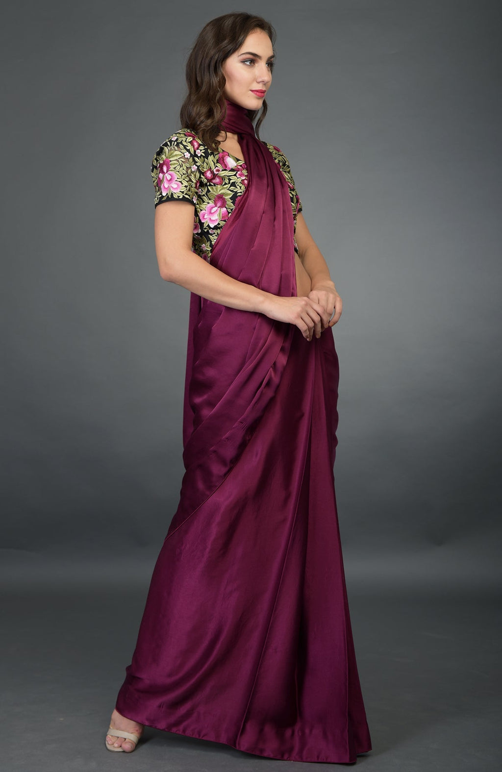 A woman models a plum satin silk saree with a floral embroidered black blouse.