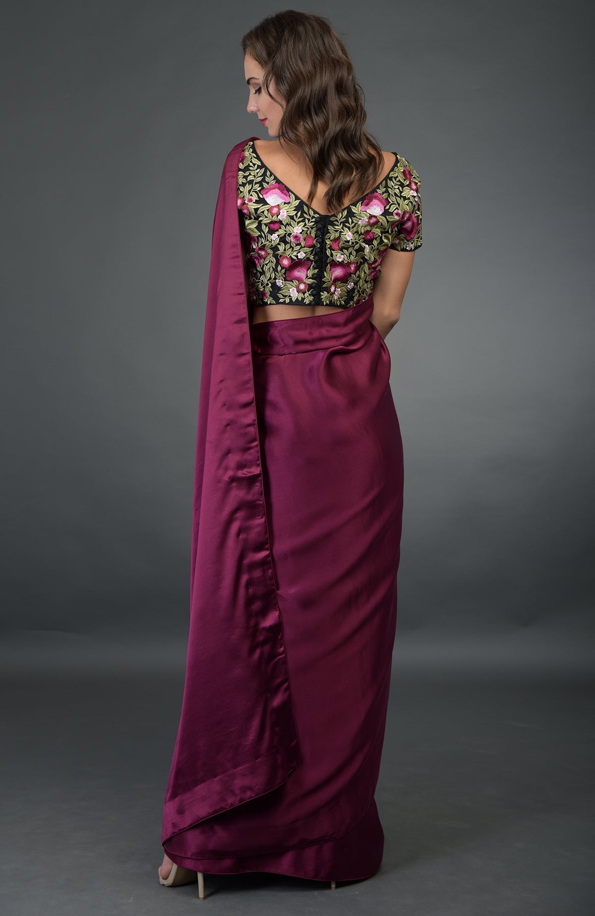 A woman models a plum saree with a black floral embroidered blouse from the back.