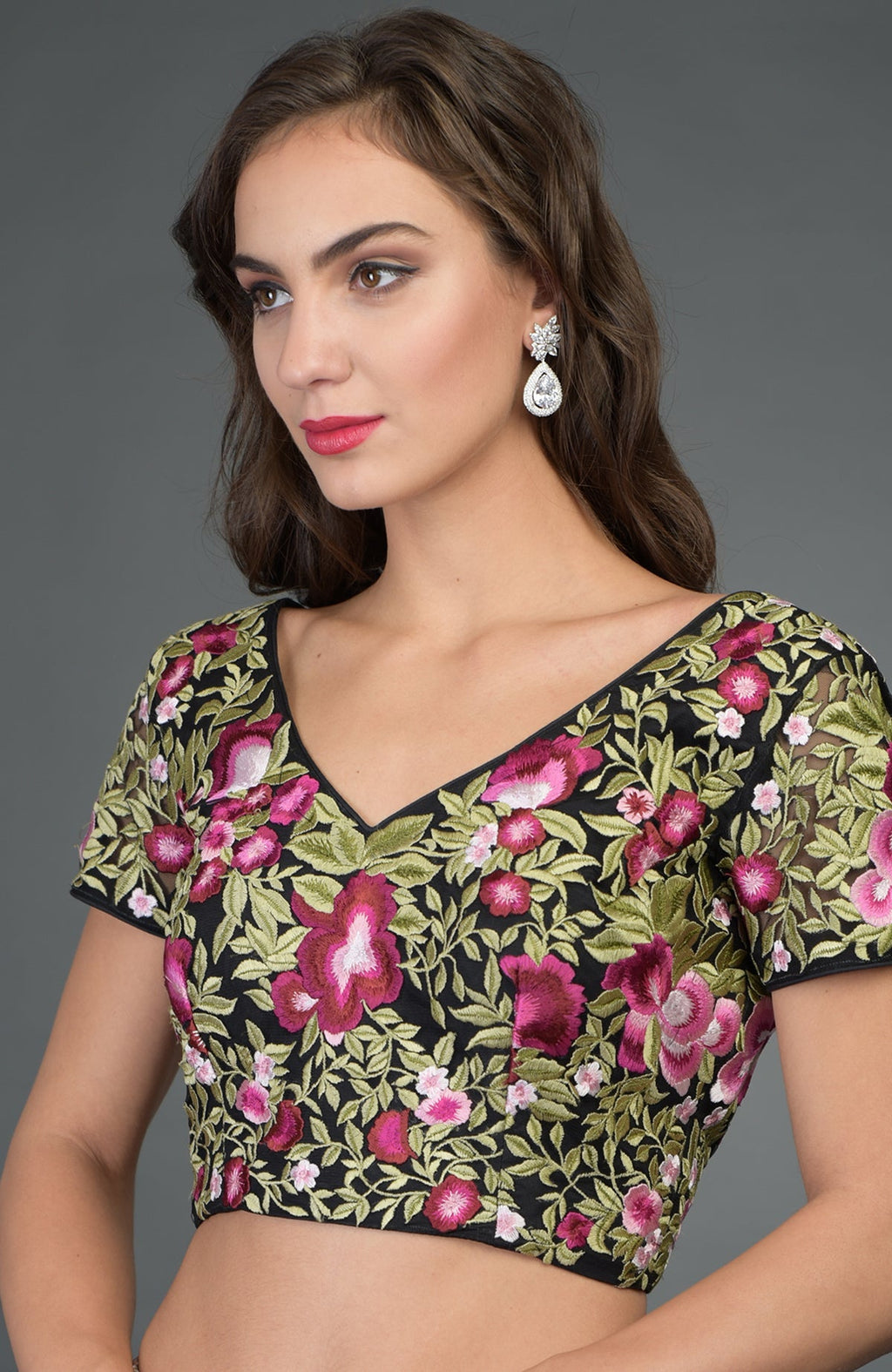 A woman models a black floral embroidered blouse with a V-neckline and cap sleeves.