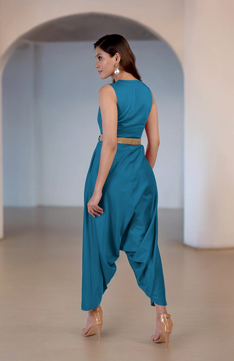 A woman models a teal V-neck jumpsuit with an embroidered belt and afgani-style pants.
