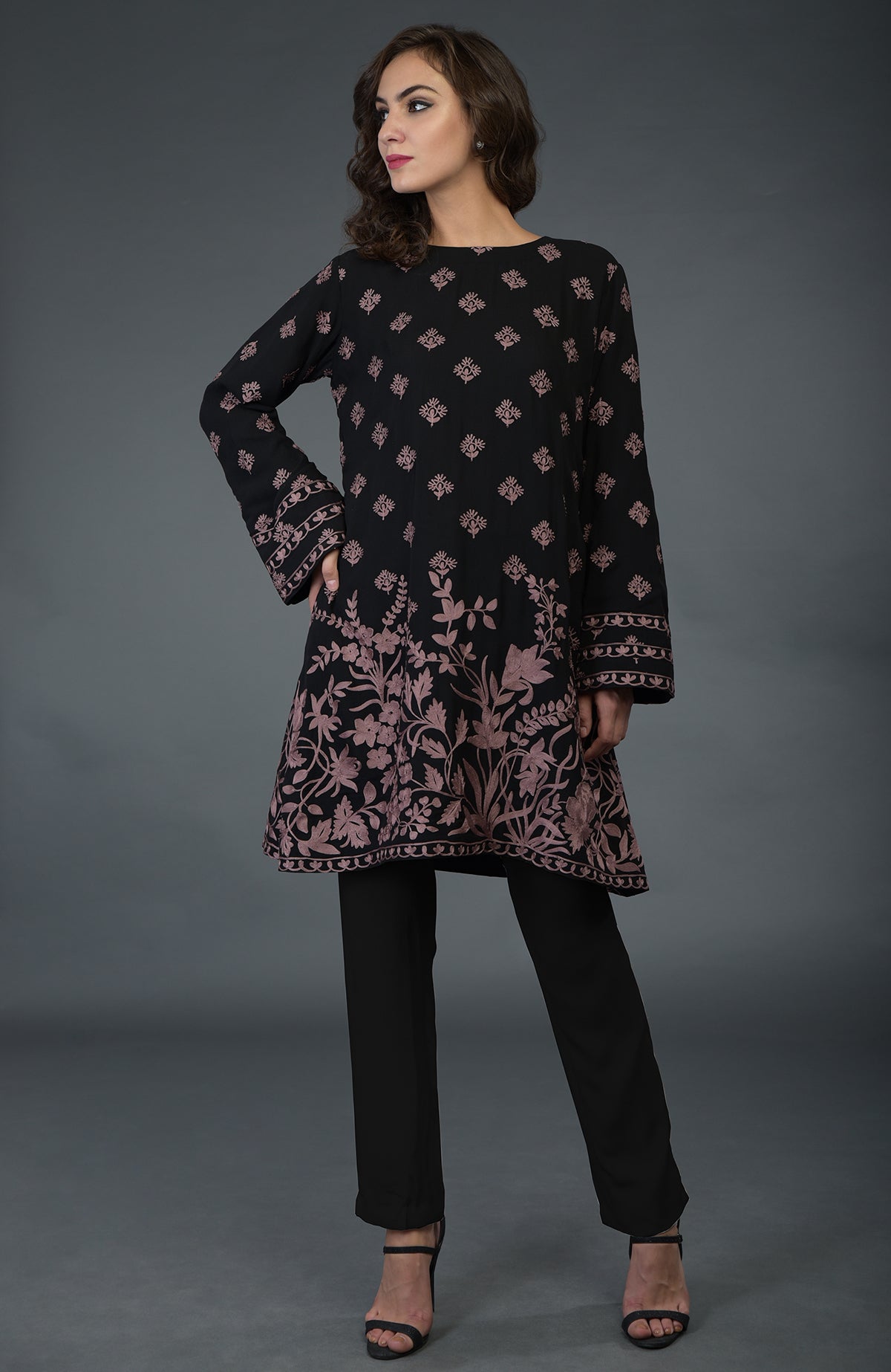 A woman models a black tunic with mauve Parsi embroidery and black pants.