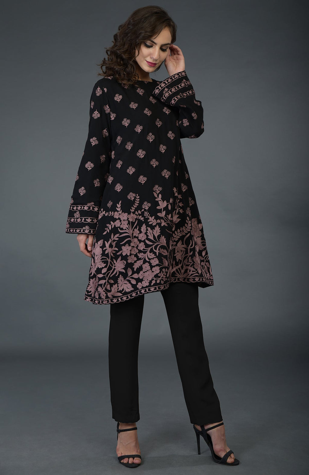 A woman models a black-mauve Parsi embroidered tunic suit with black pants and heels.