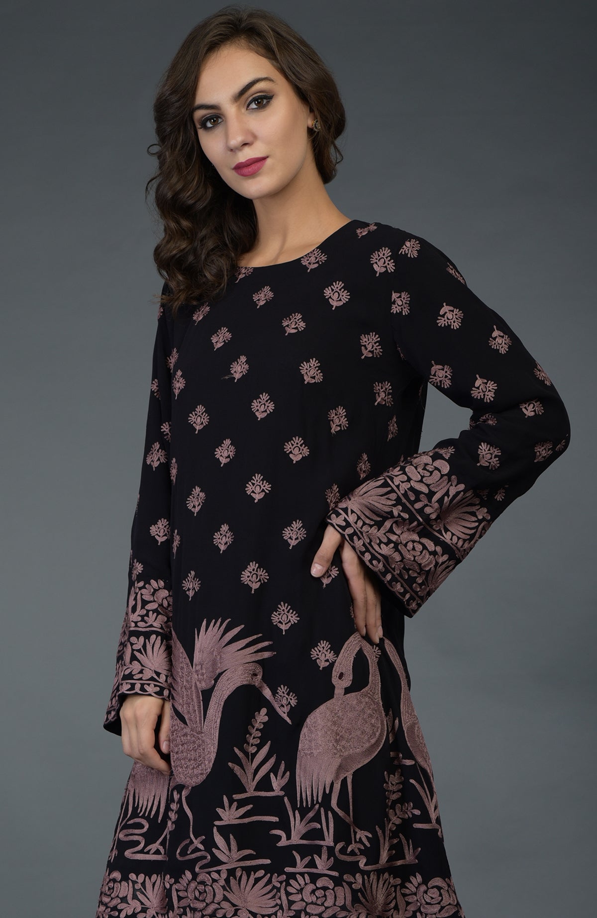 A woman models a black tunic with mauve Parsi embroidery and crane motifs.