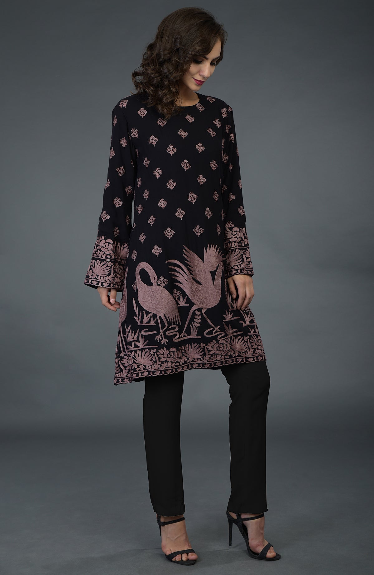 A woman models a black tunic with mauve Parsi embroidery and black pants.