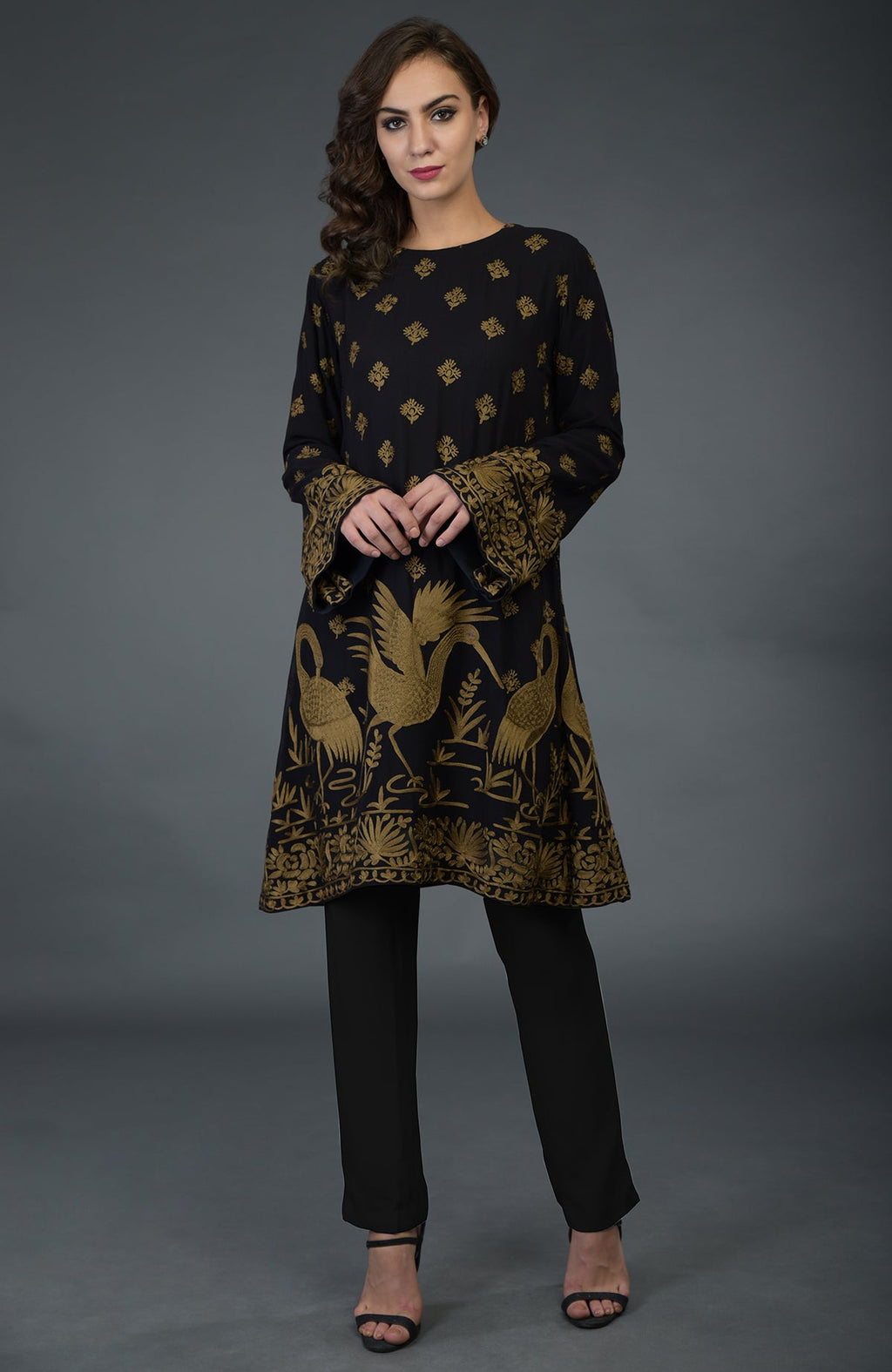 A woman models a black tunic with gold Parsi embroidery and matching pants.