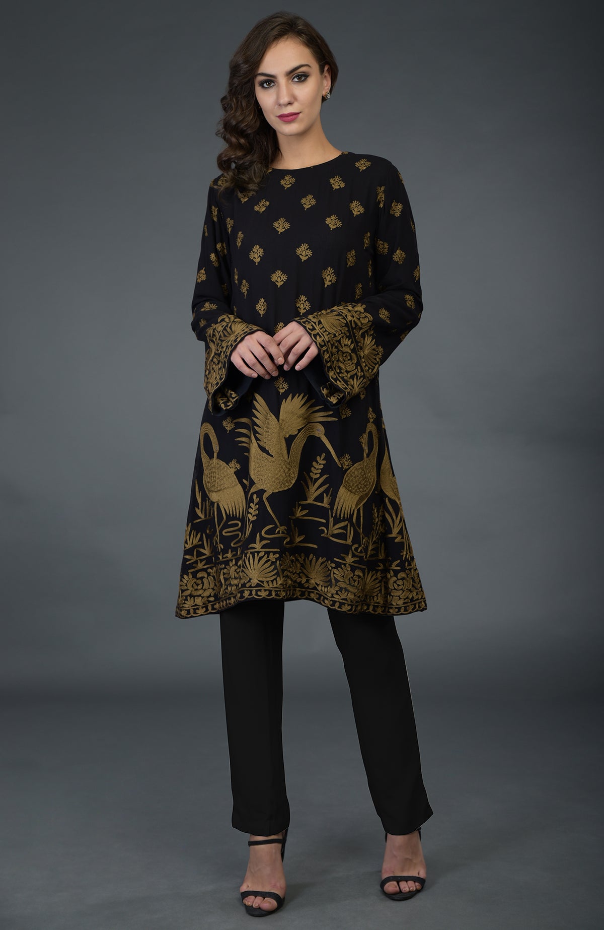 A woman models a black tunic with gold Parsi embroidery and matching pants.