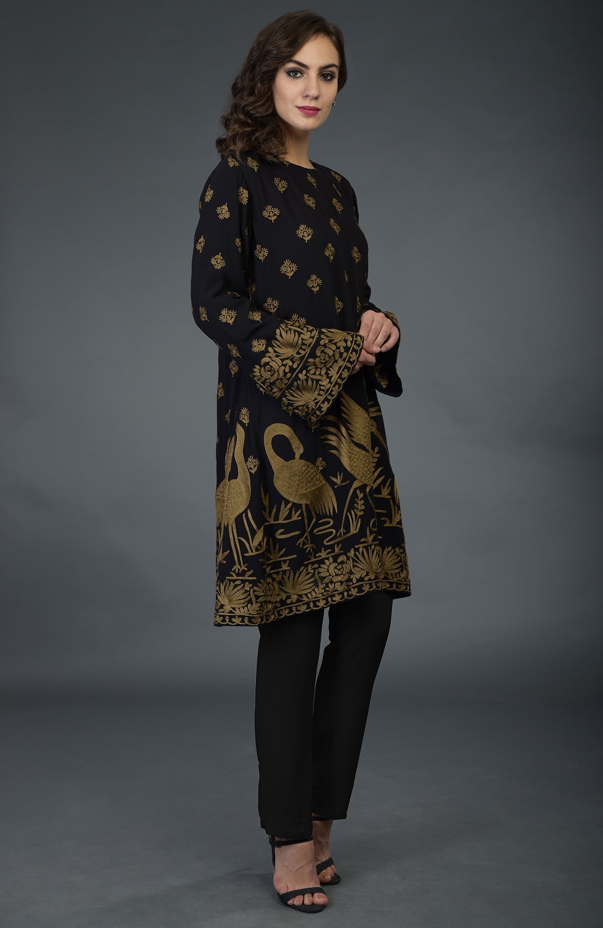 A woman models a black tunic with gold Parsi embroidery and matching pants.