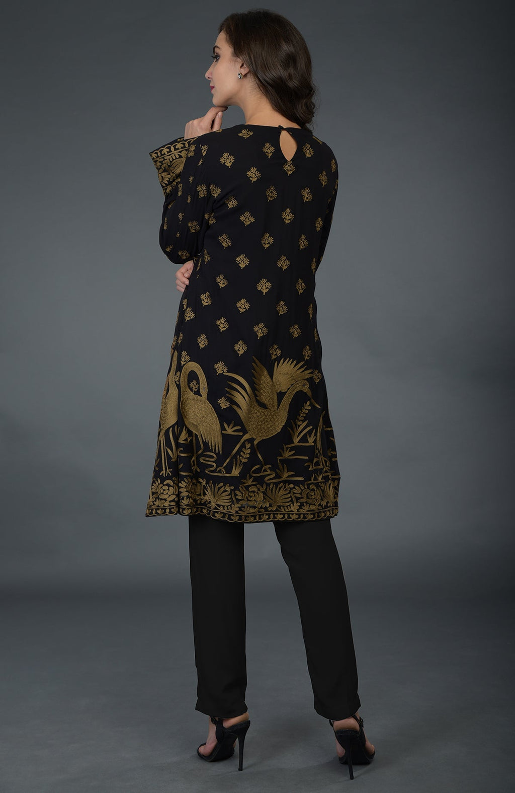 A woman models a black tunic with gold Parsi embroidery and matching pants.