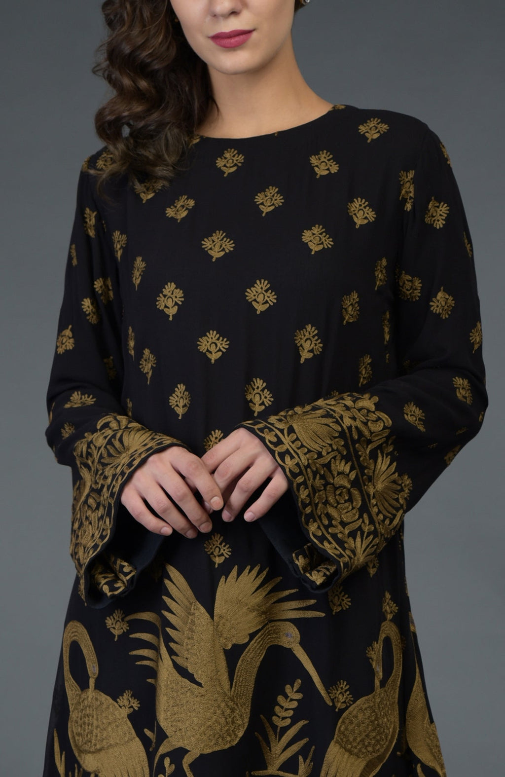 A woman models a black tunic with gold Parsi embroidery and bell sleeves.