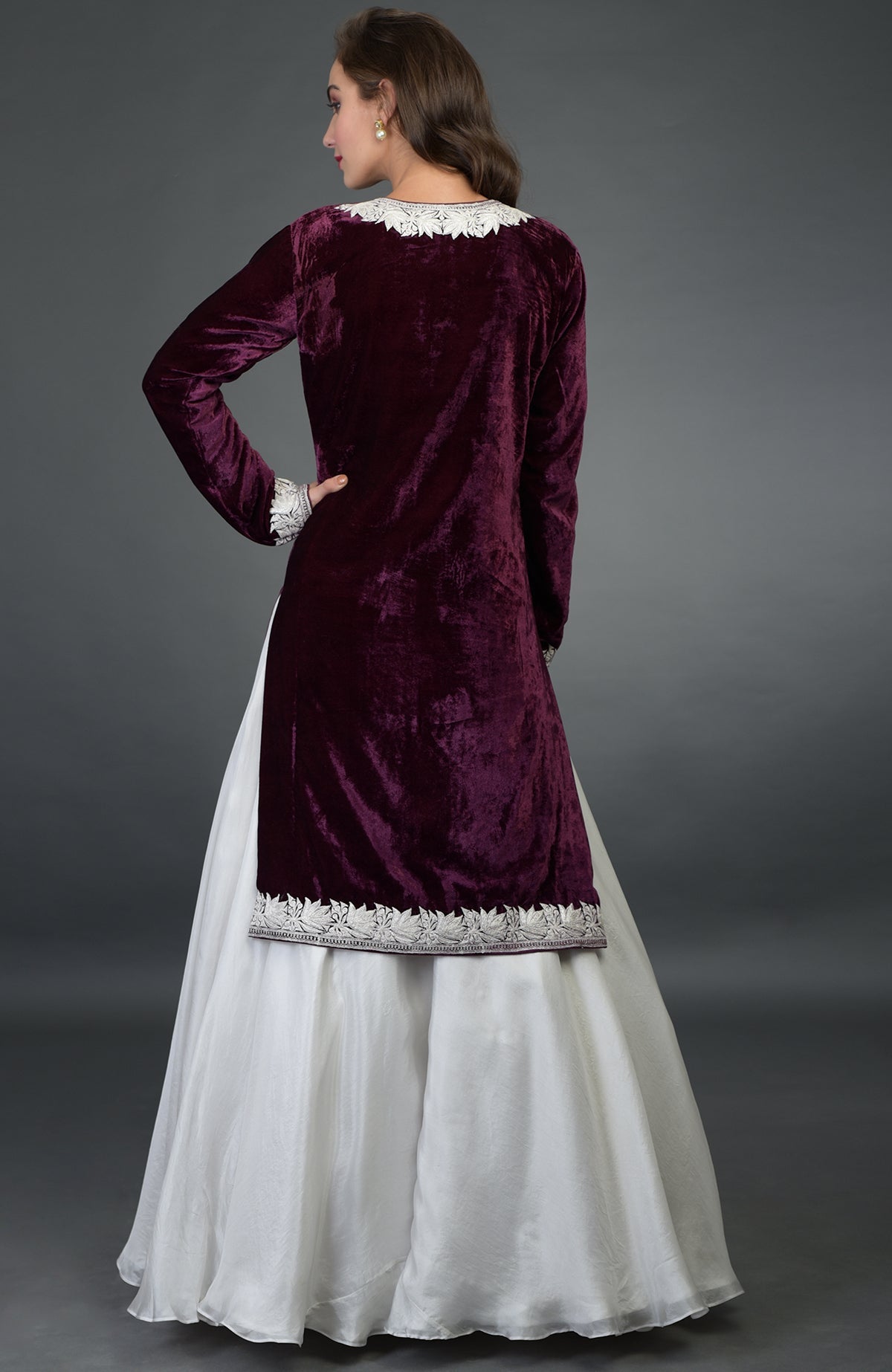 A woman from behind wears a plum velvet kurta with white embroidery and a white skirt.