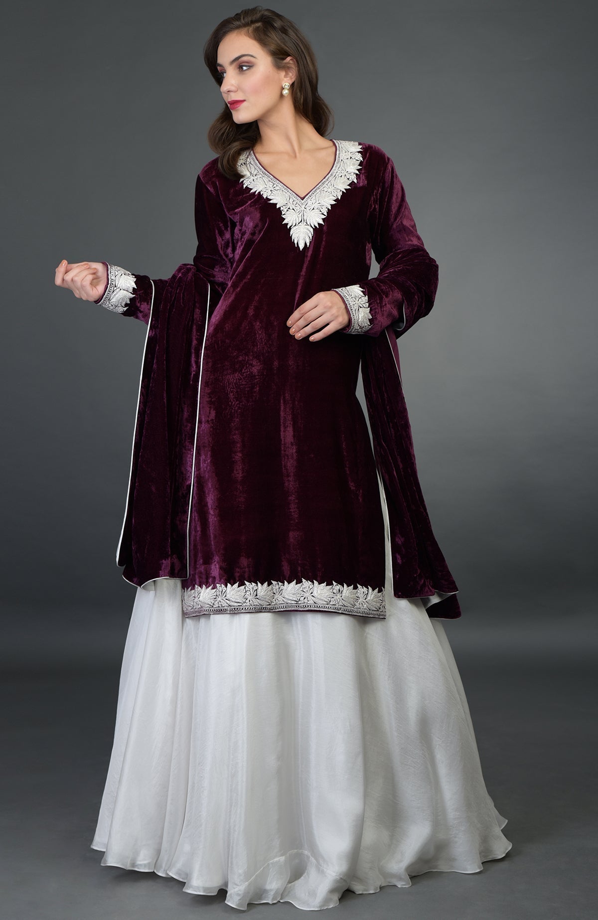 A woman models a plum velvet kurta with silver embroidery, a white skirt, and a matching dupatta.