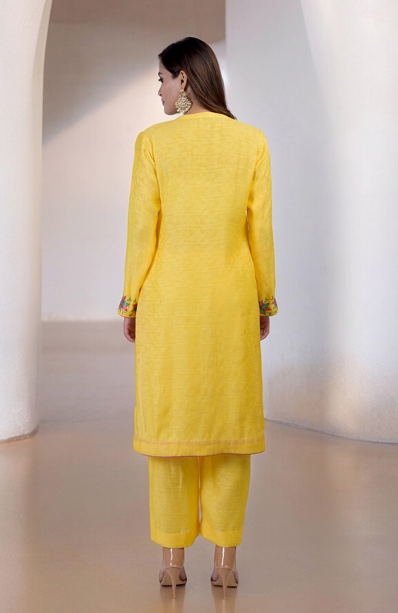 A woman from behind wears a yellow Phulkari embroidered kurta set with wide-leg pants.