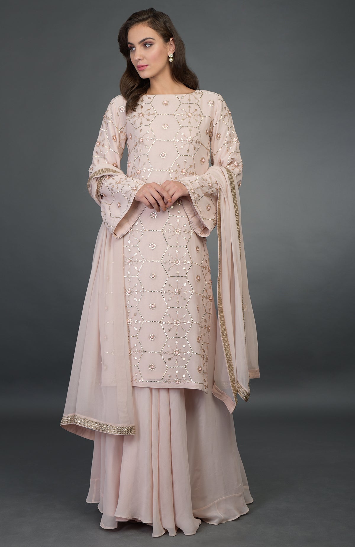 A woman models a nude pink suit with rose gold gota patti embroidery and a dupatta.