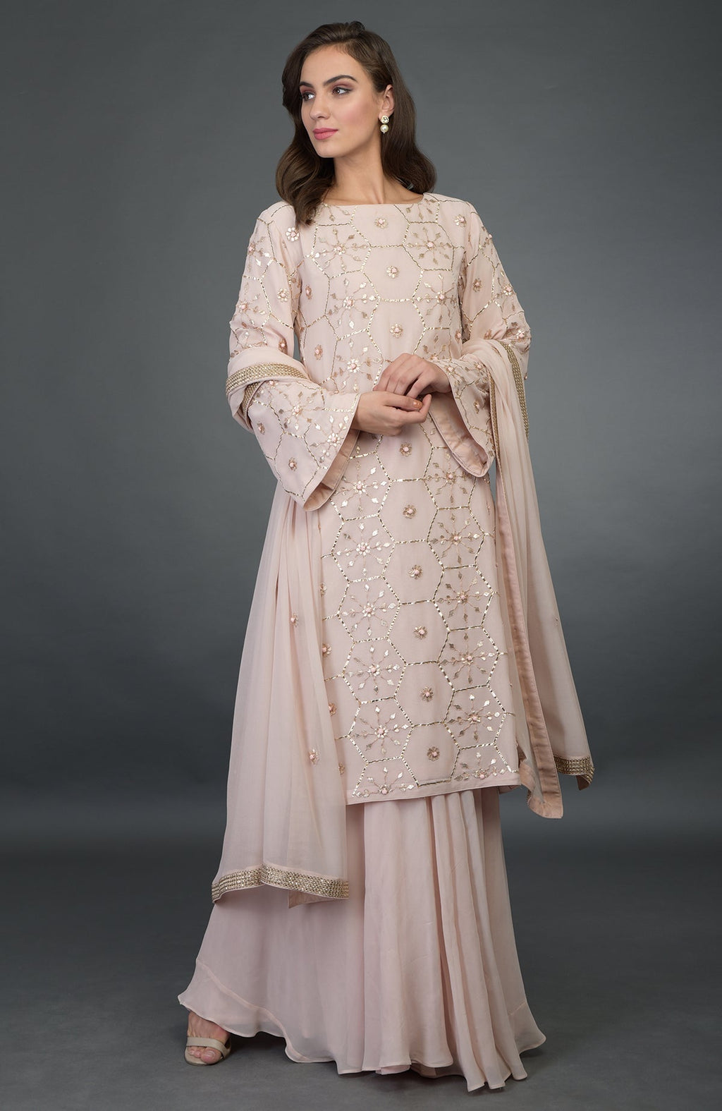 A woman models a nude pink suit with rose gold gota patti work and a dupatta.