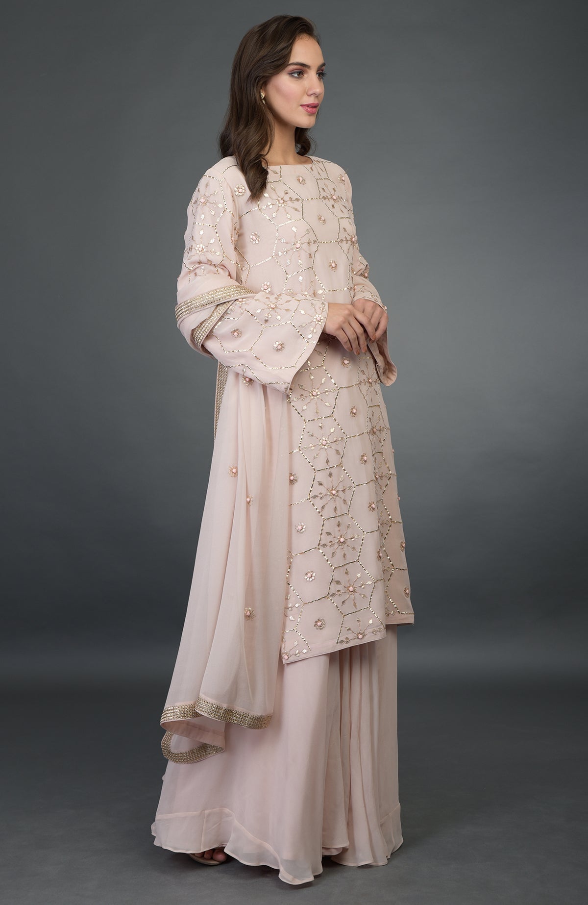 A woman models a nude pink suit with rose gold gota patti work and a dupatta.