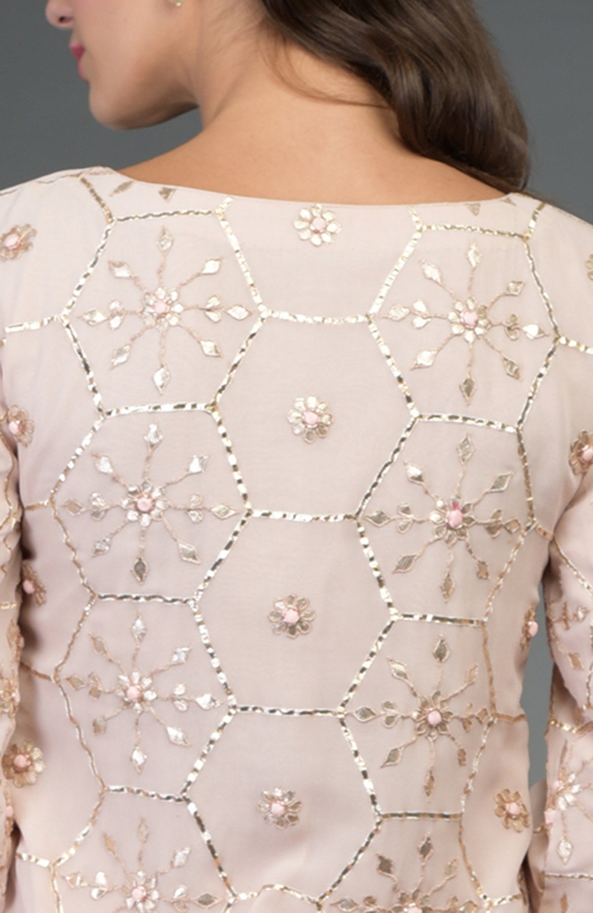 A woman models the back of a nude pink suit with rose gold gota patti embroidery.