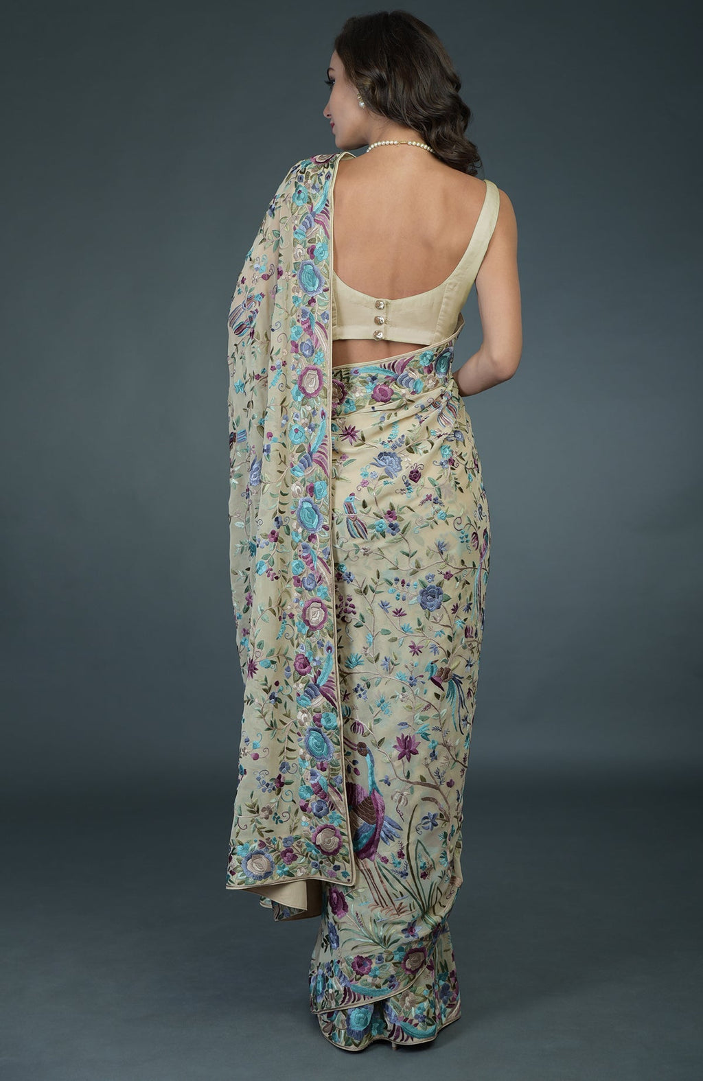 A woman from behind wears a fawn Parsi Gara hand-embroidered saree with a matching blouse.