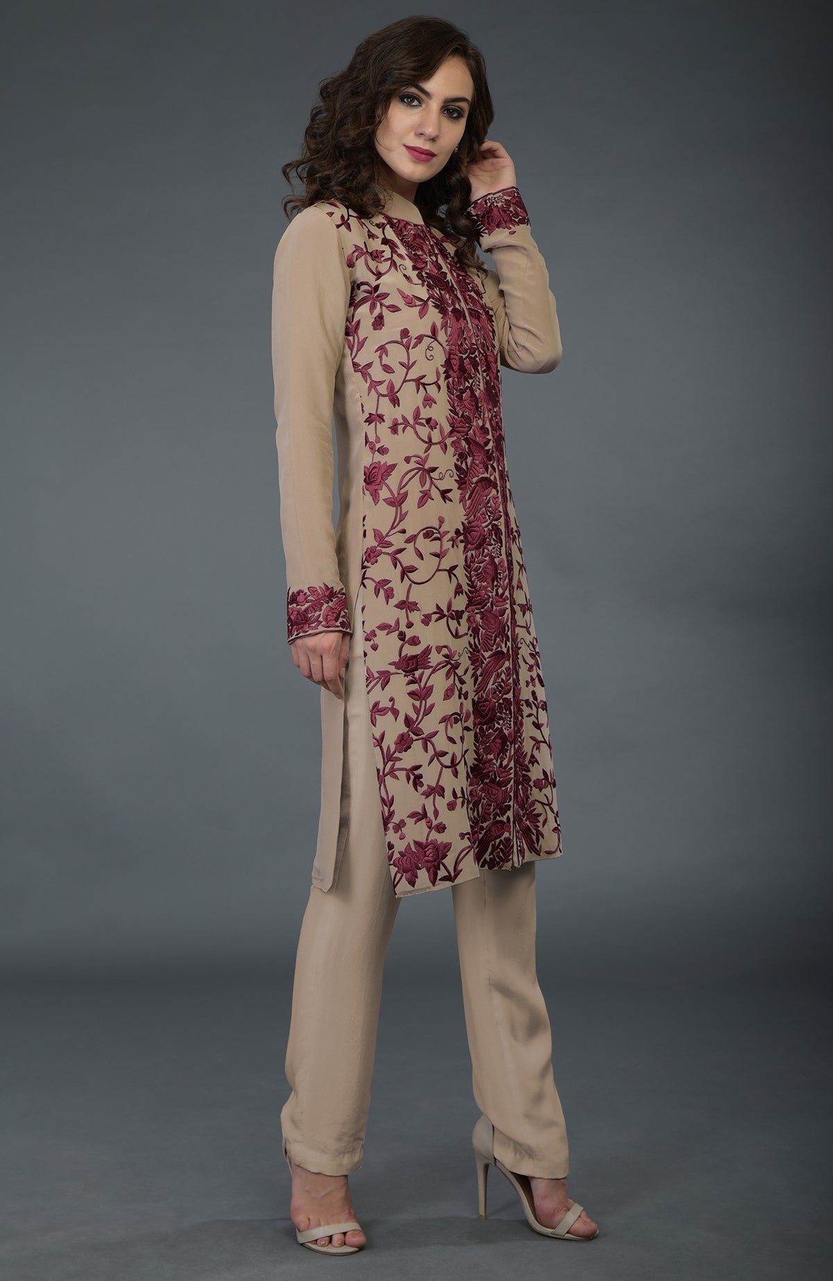 A woman models a fawn Parsi Gara jacket set with wine floral and bird embroidery.