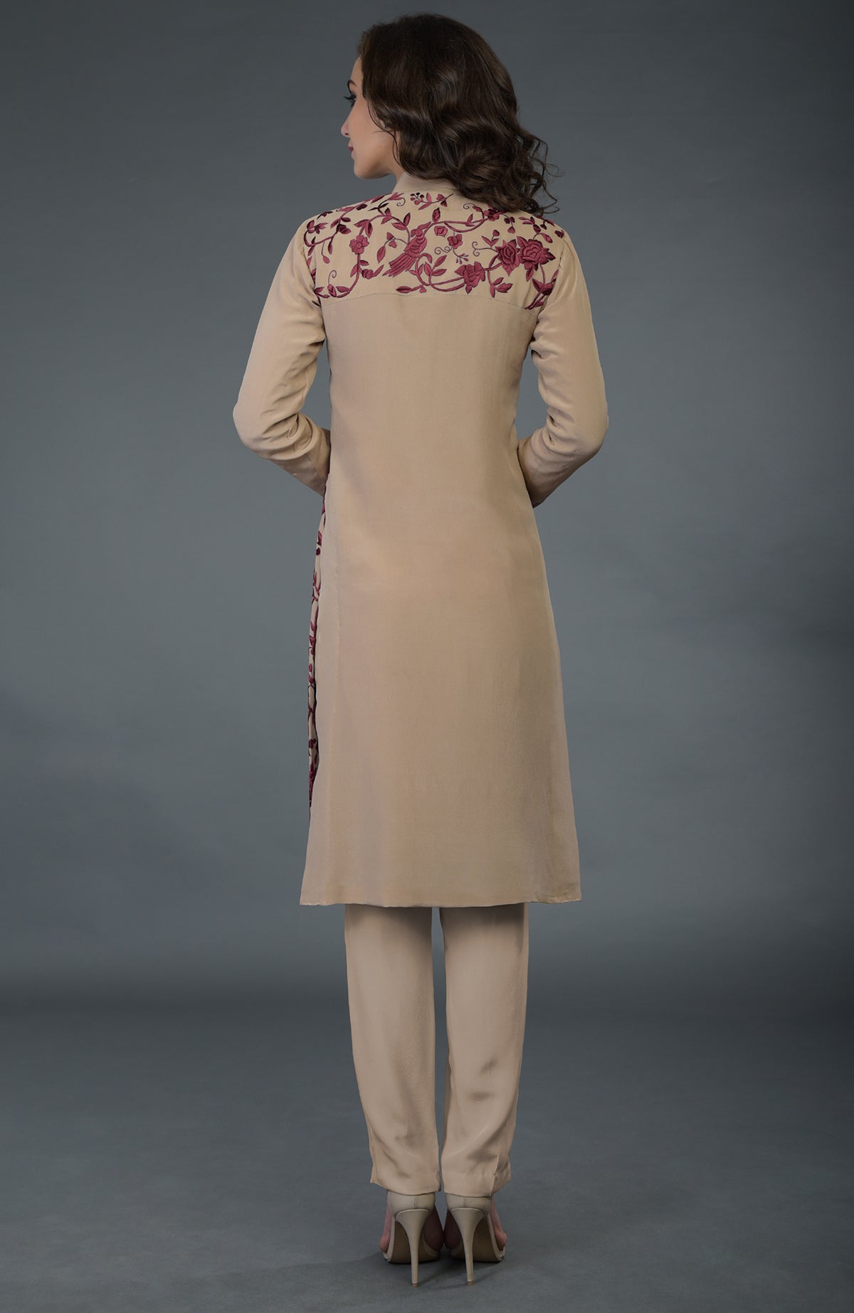A woman models a fawn Parsi Gara jacket set with wine floral and bird embroidery.