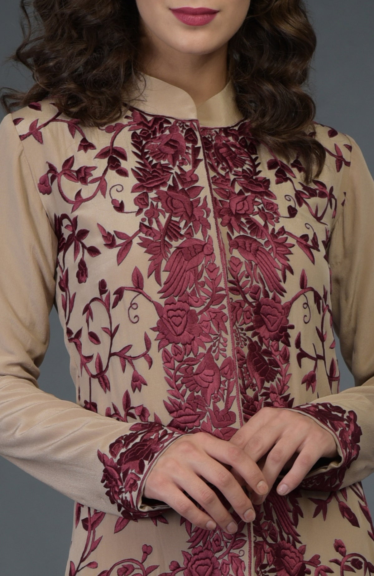 A woman wears a fawn Parsi Gara jacket with wine floral and bird embroidery.