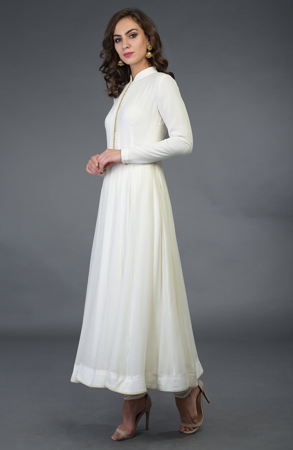 An elegant woman models an ivory anarkali suit with gold trim and matching heels.