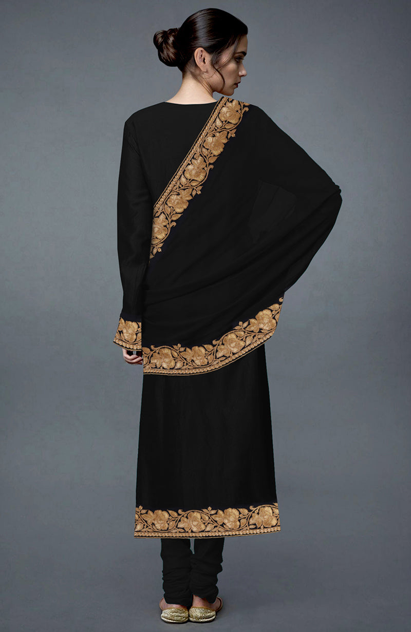 A woman from behind wears a black suit with gold floral embroidery and matching shoes.