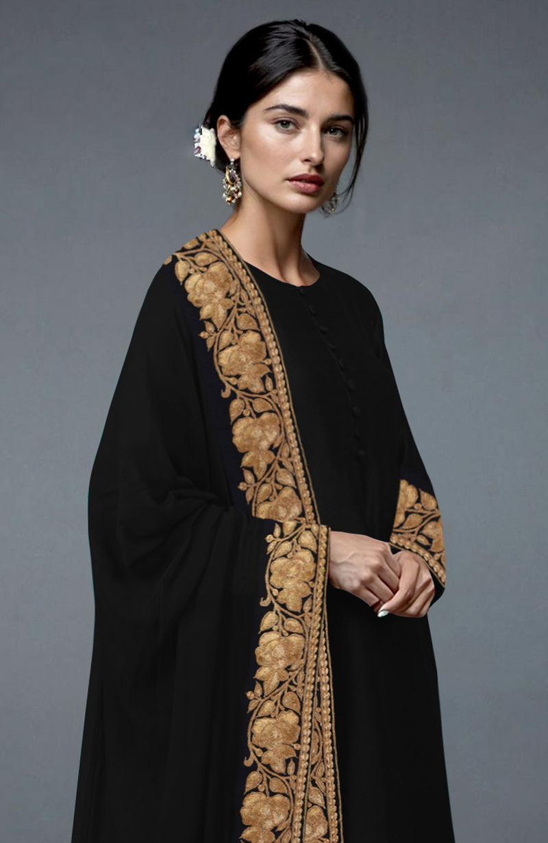 A woman models a black Kashmiri Tilla embroidered suit with gold floral patterns.