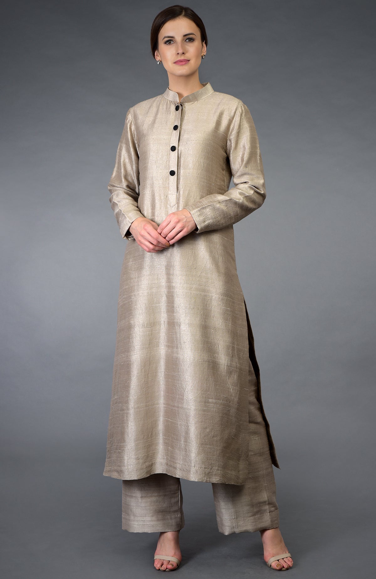 A woman models a beige raw silk suit with a band collar and black buttons.