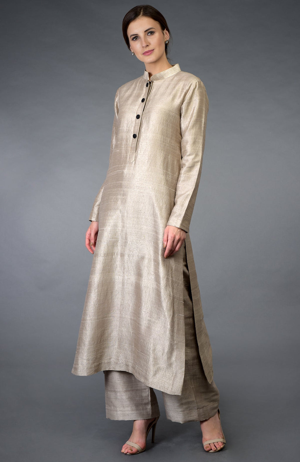 A woman models a beige raw silk suit with a band collar and black buttons.