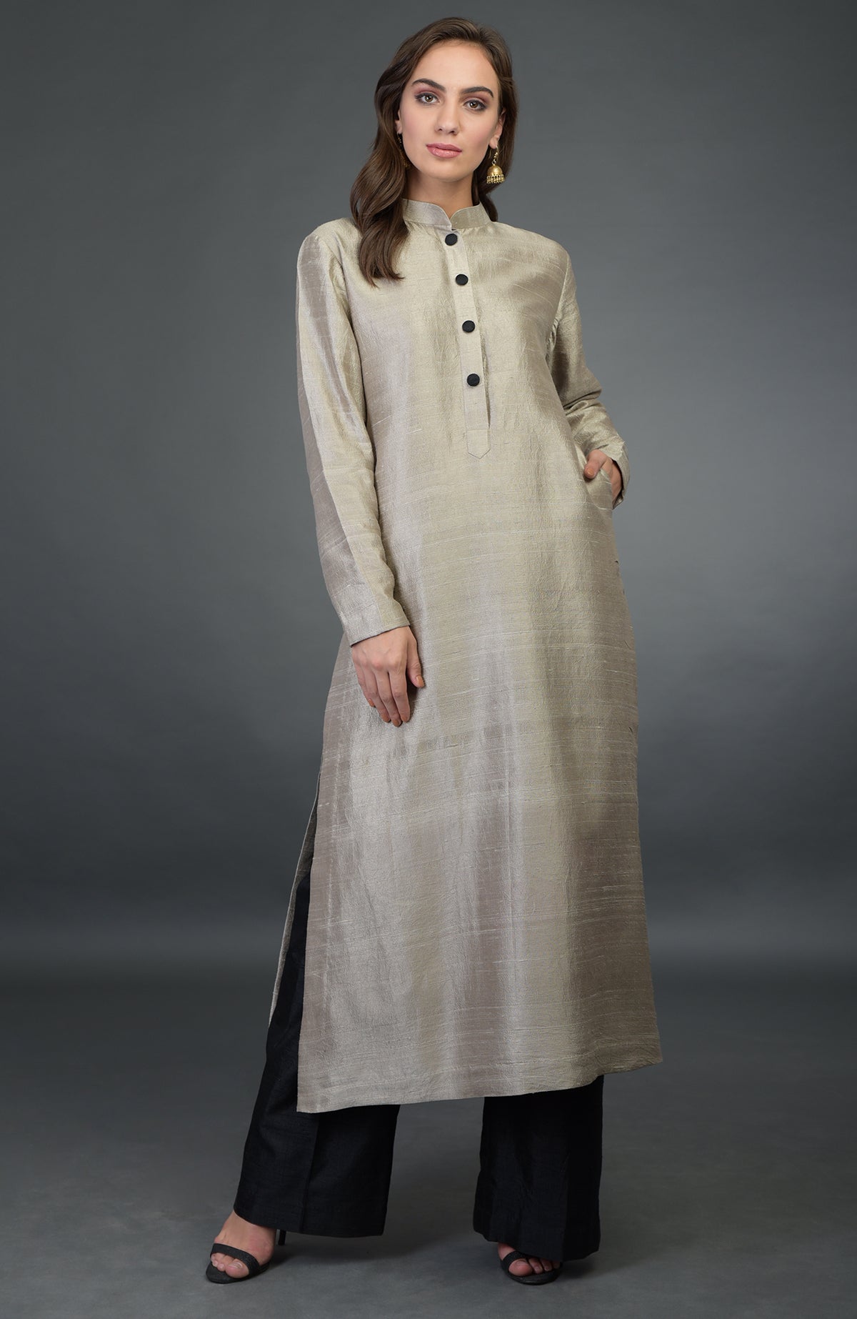 A woman models a beige raw silk kurta with black buttons and black wide-leg pants.