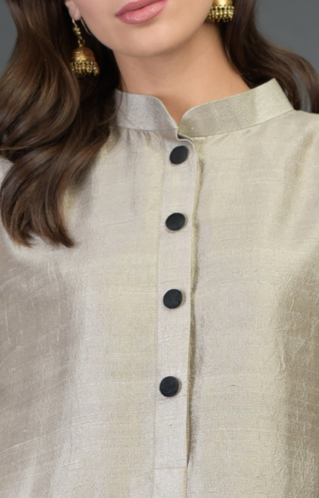 A woman wears a beige raw silk suit with a band collar and black buttons.