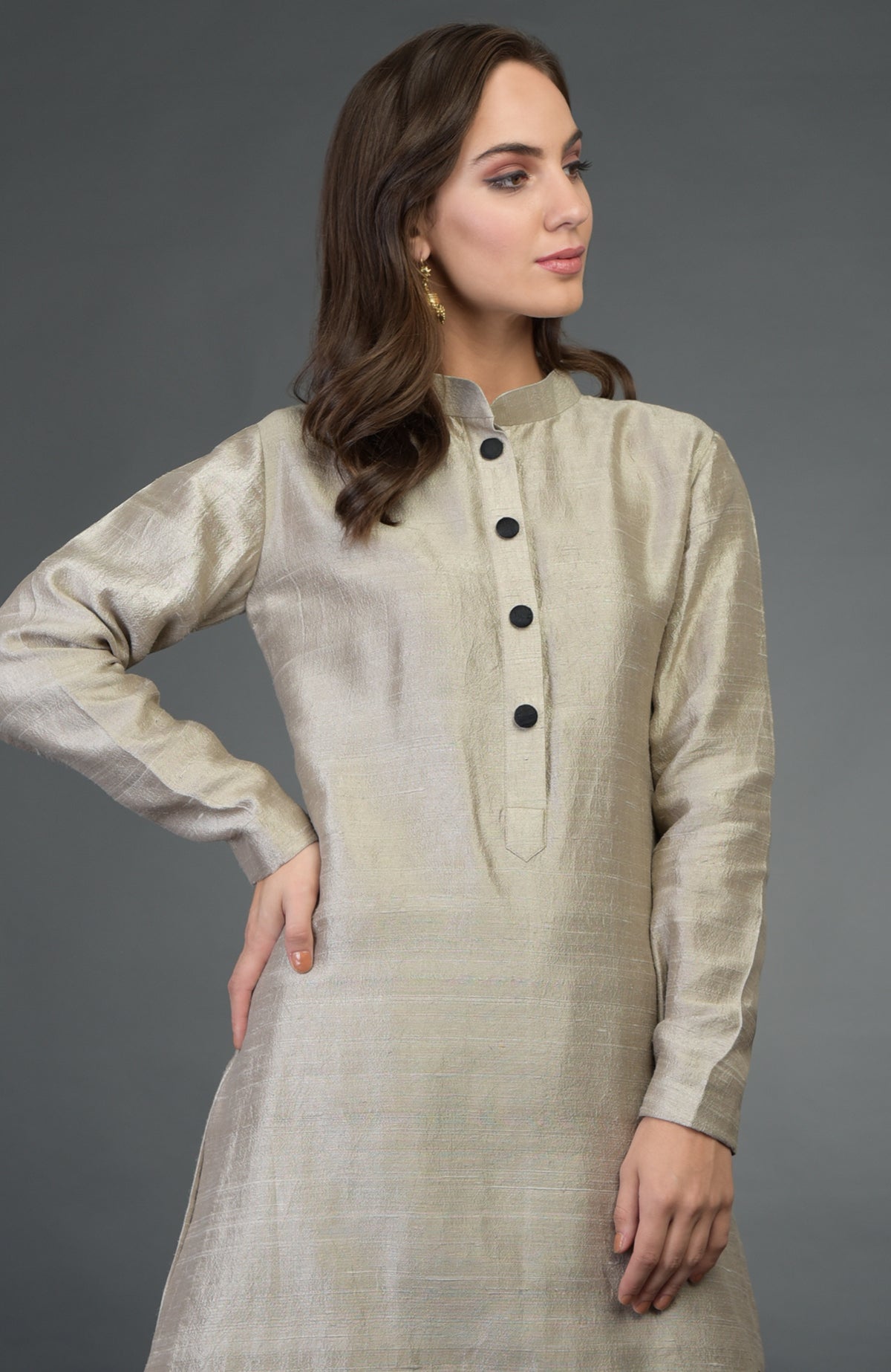 A woman models a beige raw silk suit with a band collar and black buttons.