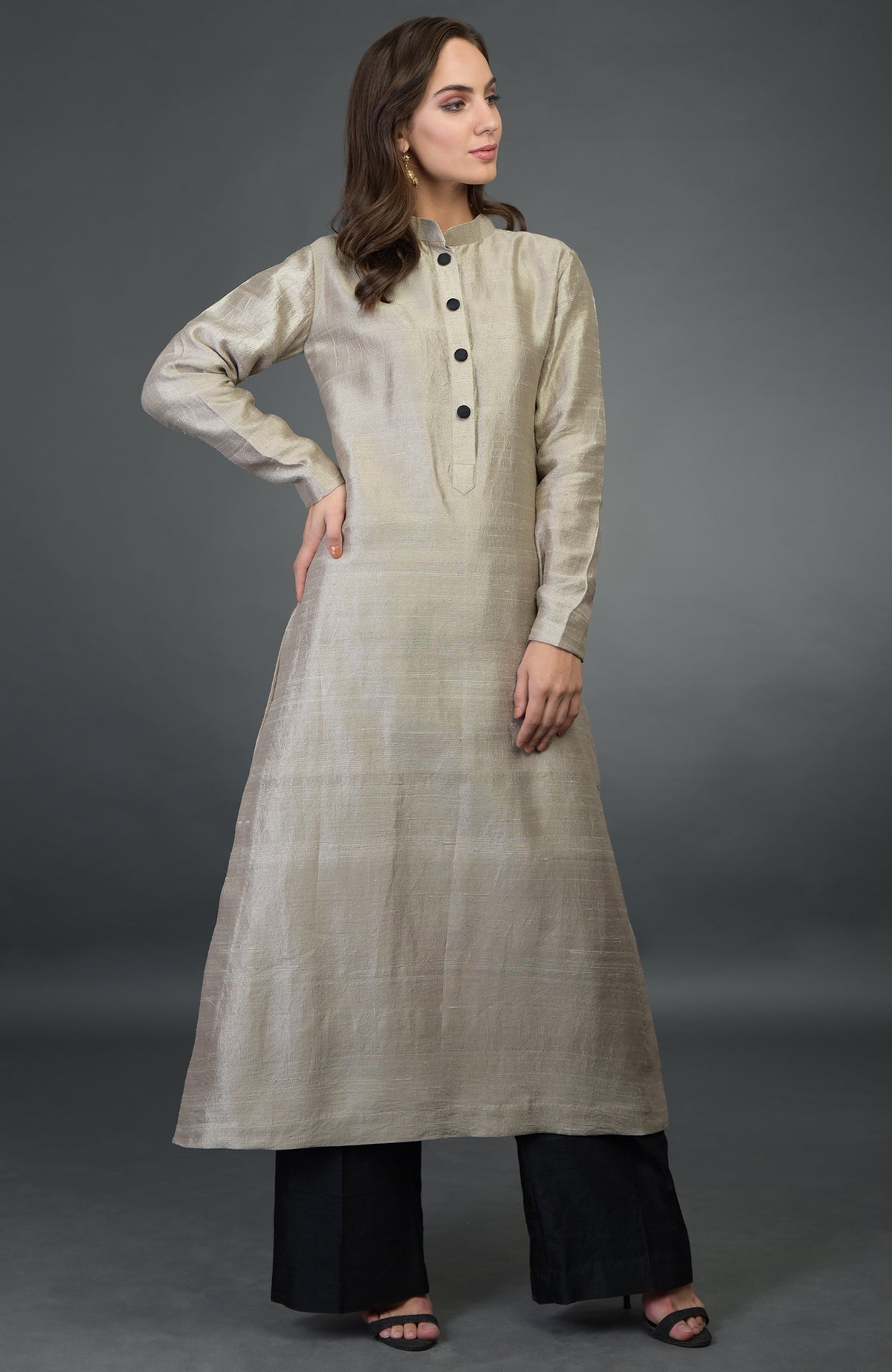 A woman models a beige raw silk suit with black buttons and black wide-leg pants.