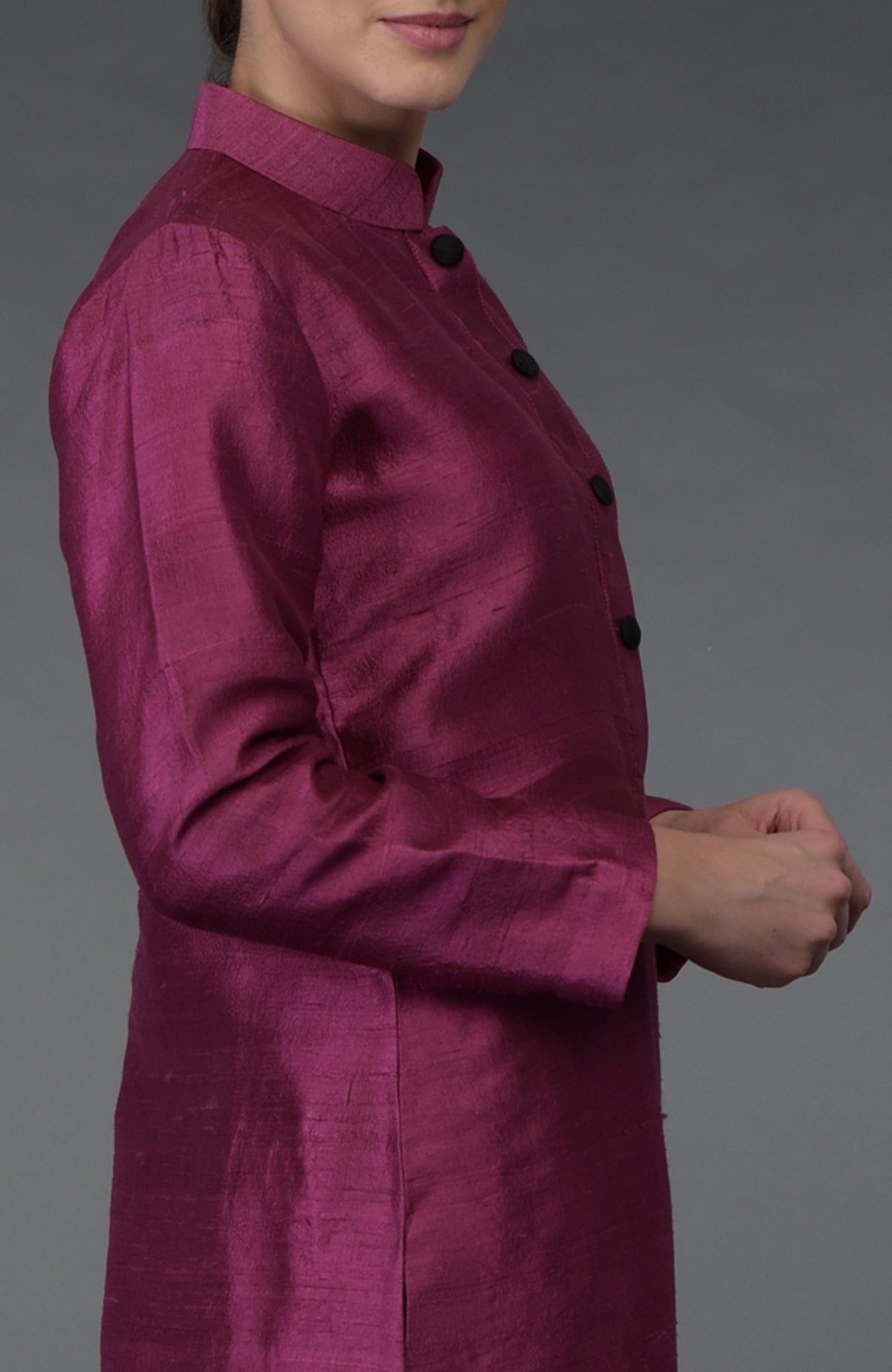 A woman wears a peacock pink raw silk suit with a band collar and black buttons.