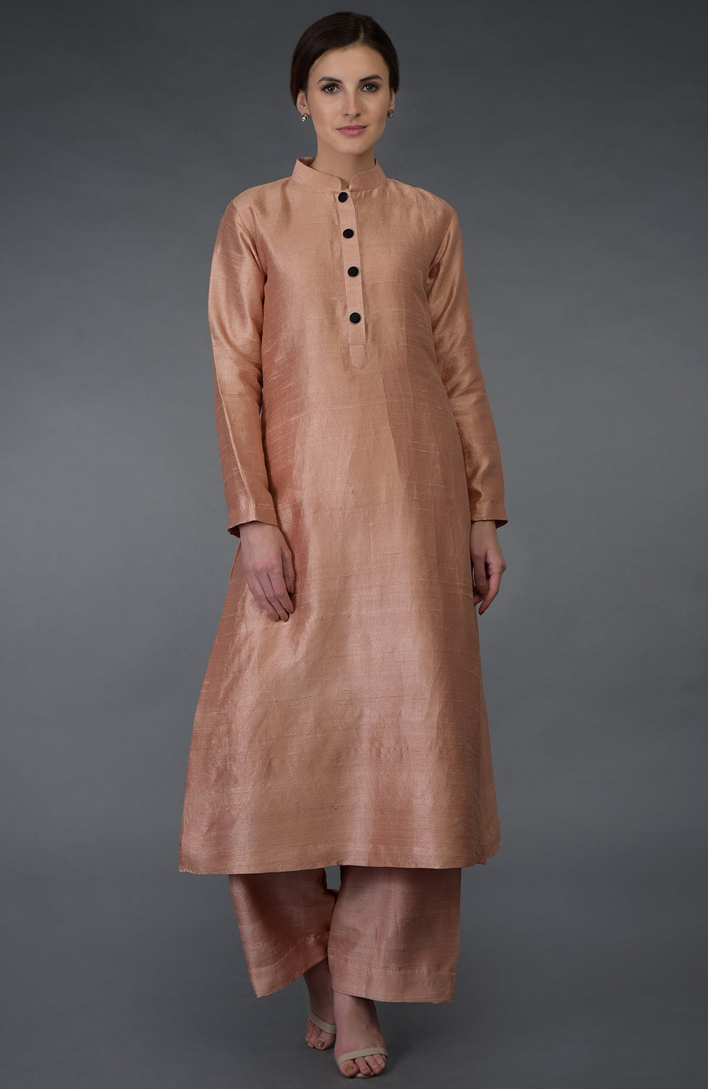 A woman models a pressed rose raw silk suit with a band collar and black buttons.
