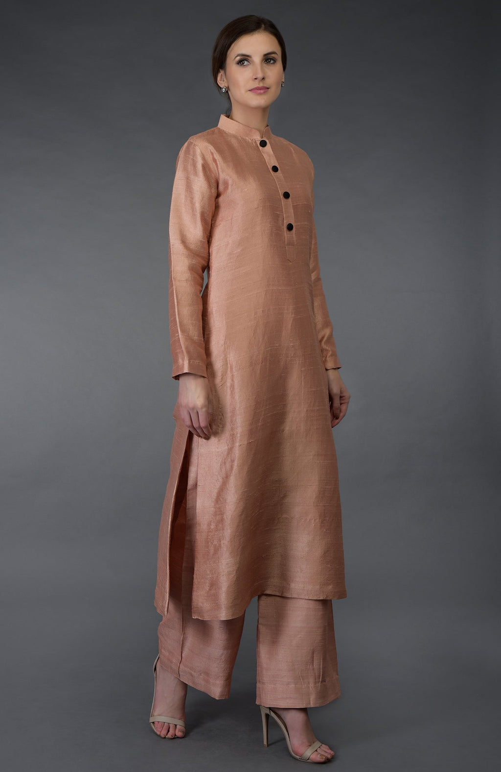 A woman models a pressed rose raw silk suit with a band collar and black buttons.