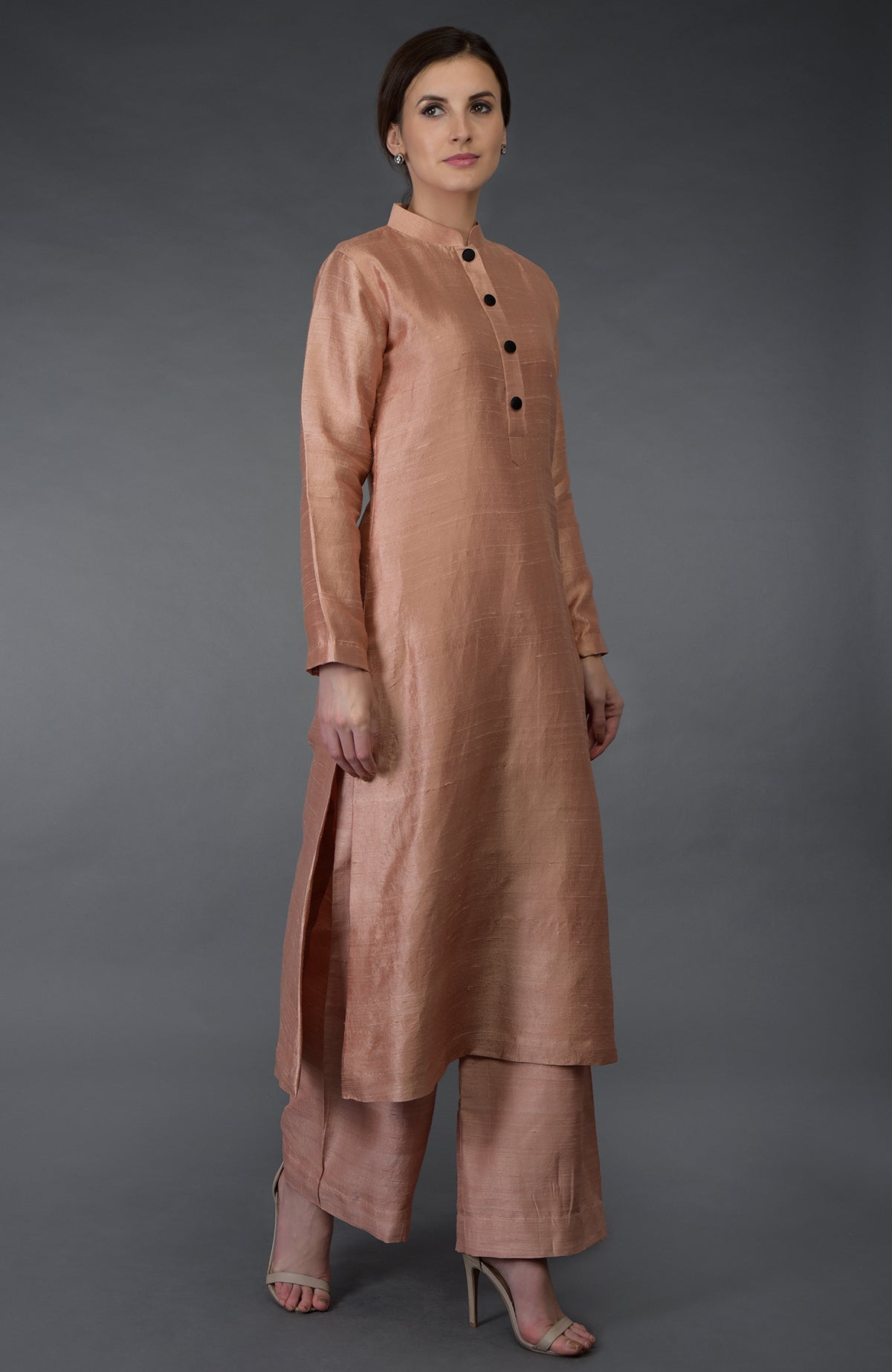 A woman models a pressed rose raw silk suit with a band collar and black buttons.